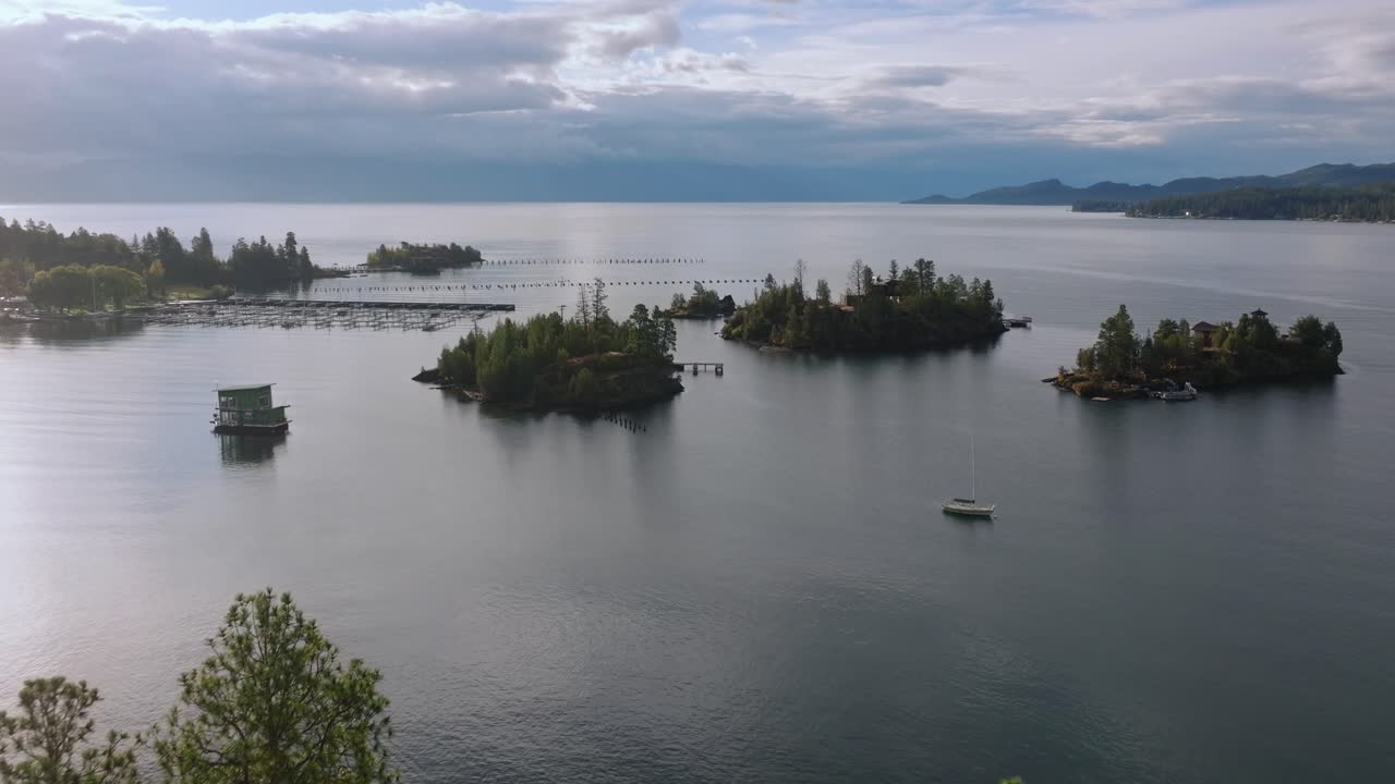 Flathead Gölü, Montana, ABD'de, tekne iskelesi marinalarının yakınında, durgun göl suyuyla çevrili ve yüzeyine yansıyan yumuşak bulutlara sahip ağaçlarla kaplı adalar kümesi