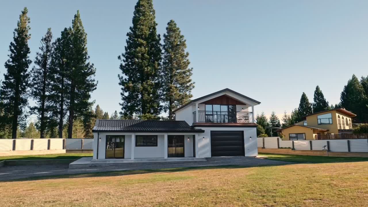 Tidsforløpsvideo som sakte zoomer ut fra et moderne, hvitt toetasjes hus med garasje, gjerde og plen i et skogkledd boligområde under en klar himmel.