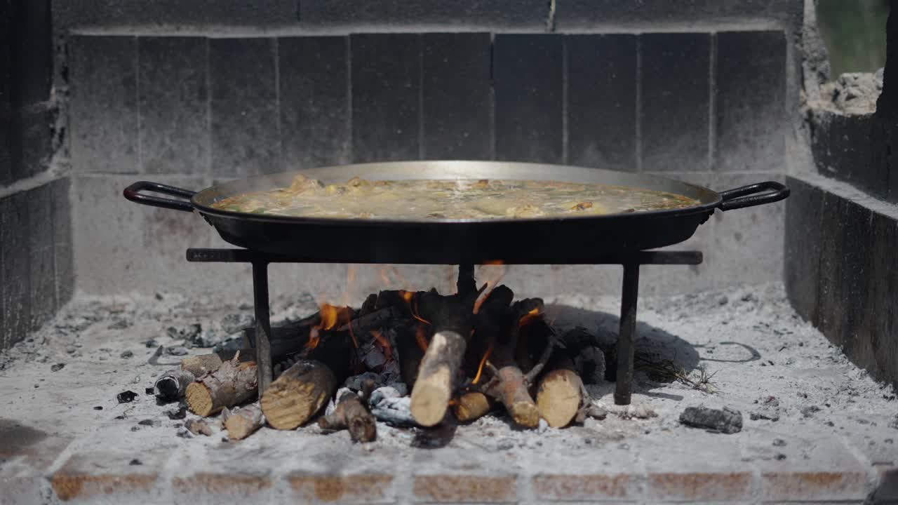 Large paella pan cooking over an open wood fire