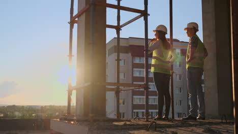 Builders-look-at-a-cityscape-on-a-sunset-background-back-view.