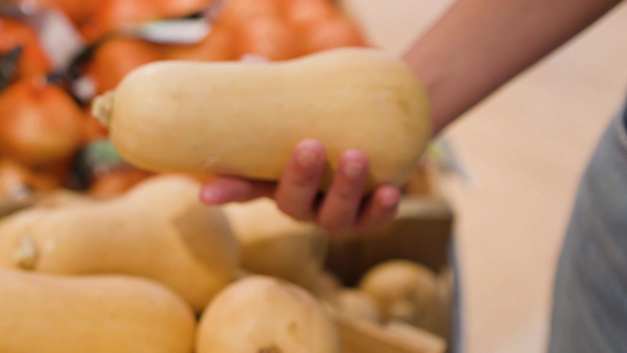 Mão escolhendo abóbora-manteiga de um expositor de produtos frescos