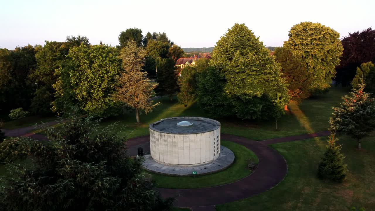Aerial view circling peaceful crematorium tomb chamber in partially sunrise sunlit garden woodland