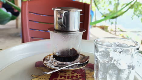 vietnamese iced coffee at an outdoor cafe in vietnam. phin filter brews hot coffee next to a glass of ice. relaxing, authentic coffee experience.
