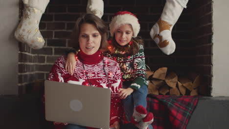 Glückliche-Mutter-Und-Tochter-In-Weihnachtspullovern-Und-Mit-Lichtern-Um-Den-Hals-Sitzen-Auf-Dem-Sofa,-Während-Sie-Den-Laptop-Benutzen-1