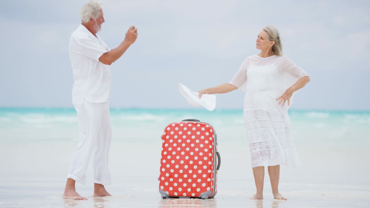 una pareja jubilada en la playa con una maleta y una cámara.