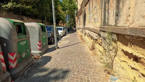 cars passing by bins on a narrow street