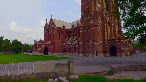 A-beautiful-old-Church-low-angle-view-by-drone,-Green-trees-and-grass-around-the-Church,-Two-cars-are-parked-in-the-parking