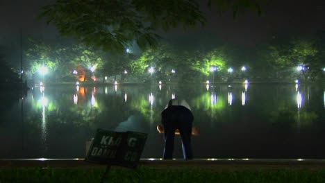 Un-Anciano-Hace-Ejercicios-De-Tai-Chi-Frente-A-Un-Lago-En-Hanoi,-Vietnam