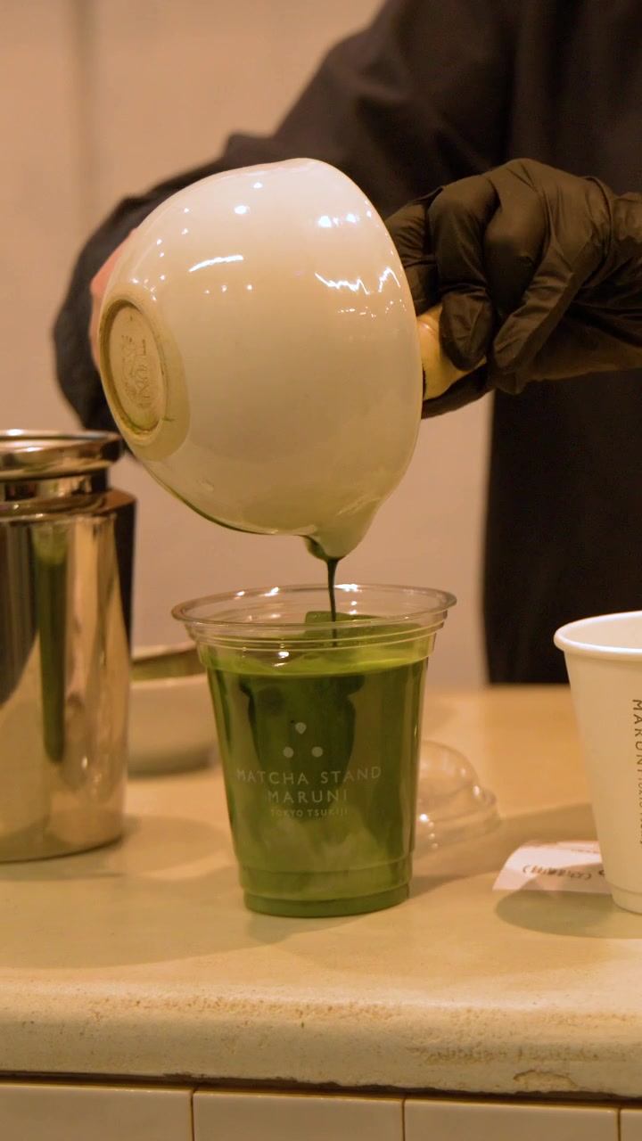 Primo piano di un barista che versa tè verde in un bicchiere di plastica con latte ghiacciato.