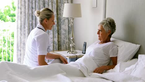 female doctor interacting with senior woman on bed in bedroom