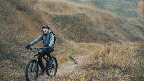 Ciclista-Masculino-Con-Casco-Montando-En-Bicicleta-De-Montaña-Por-La-Carretera-En-El-Campo