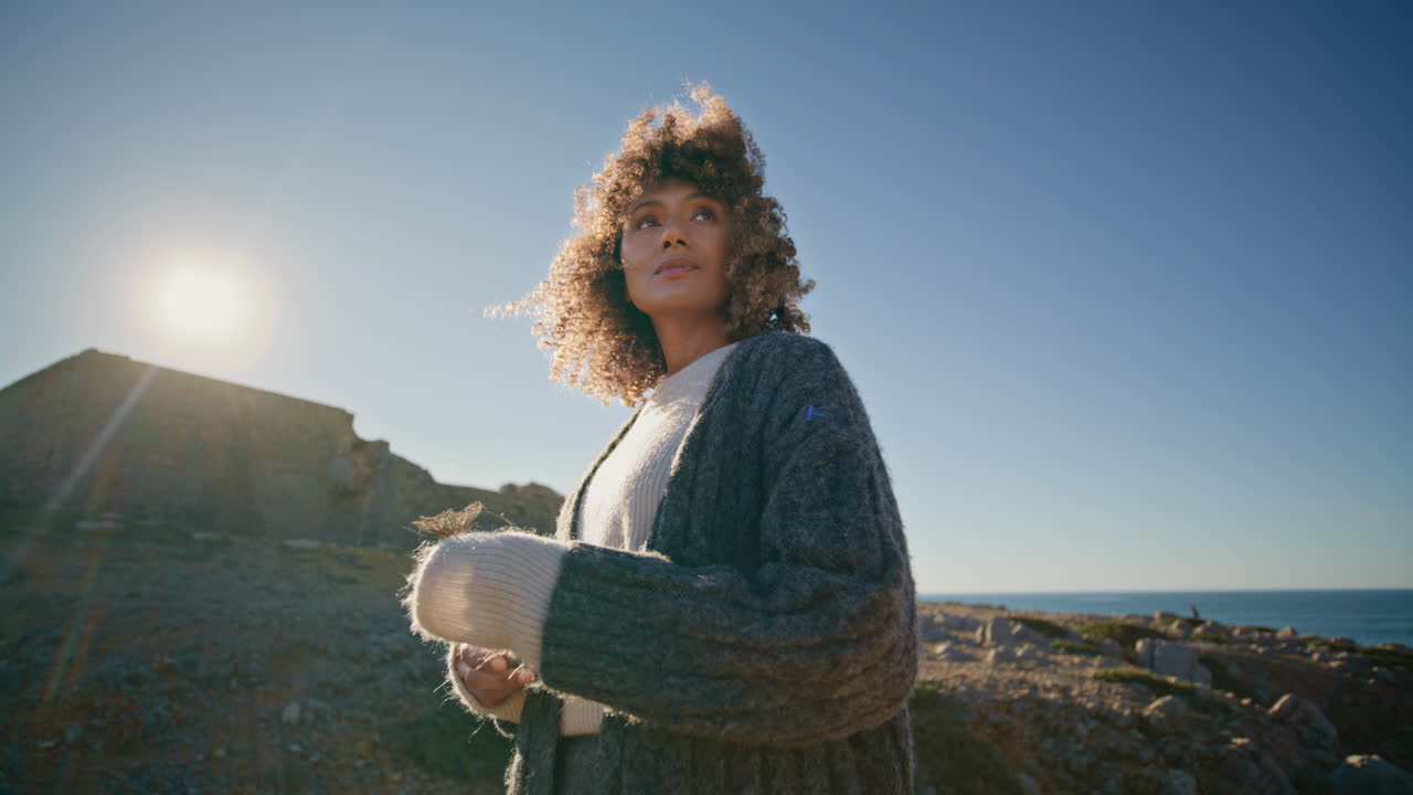 Curly woman watching cliffs walking abandoned nature. Lady holding dry flower