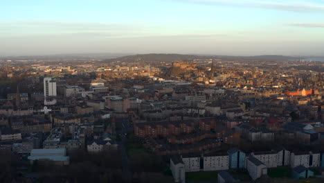 Rising-aerial-view-from-Salisbury-Crags-in-Holyrood-park-to-reveal-Edinburgh-city-as-dawn-breaks,-Scotland