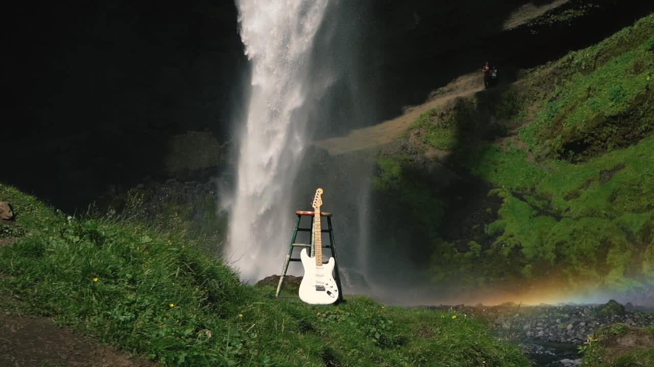 아이슬란드-7의 아름다운 폭포 앞에서 기타를 치는 남자