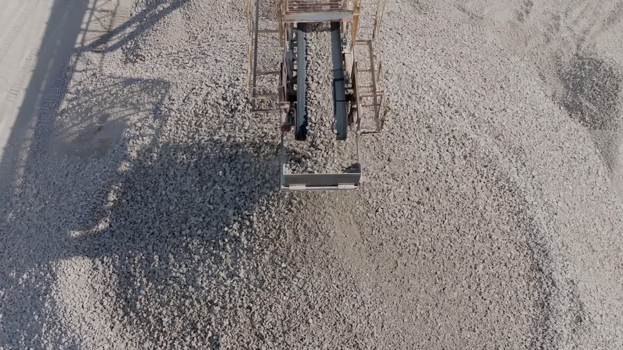 Aerial footage rotating down to reveal rocks falling off a conveyor belt into a giant pile in a quarry.