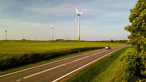 car driving on asphalt road in a wind farm with wind turbines generating green electric energy in the background