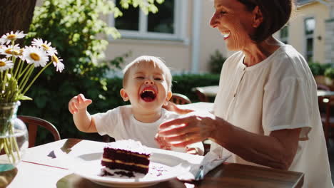 grandmother and grandchild share a joyful moment with cake at an outdoor cafe