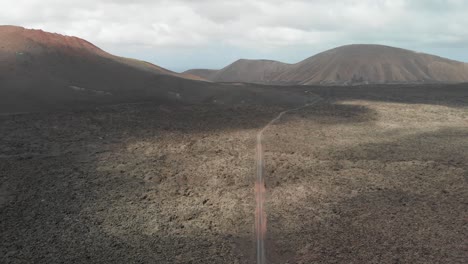 Toma-Aérea-Ascendente-Y-Giratoria-De-Un-Campo-Volcánico-Estéril-Con-Un-Camino-De-Tierra