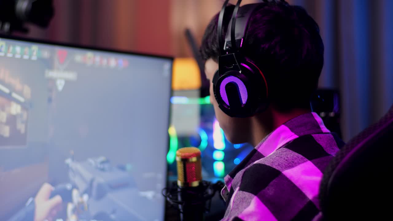 vista de atrás de un niño asiático que grita gol y baila celebrando el juego ganador a través de la red en una computadora personal. videojuego de transmisión en vivo, escritorio iluminado por luz de tira led rgb