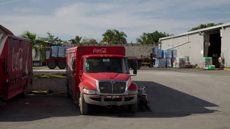 stationary parked coca cola truck at distribution centre in punta cana with fork lift workers unloading in background