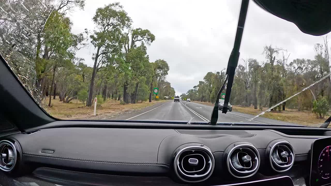 A car journey along Great Ocean Road, showcasing lush greenery and overcast skies, captured from inside a vehicle