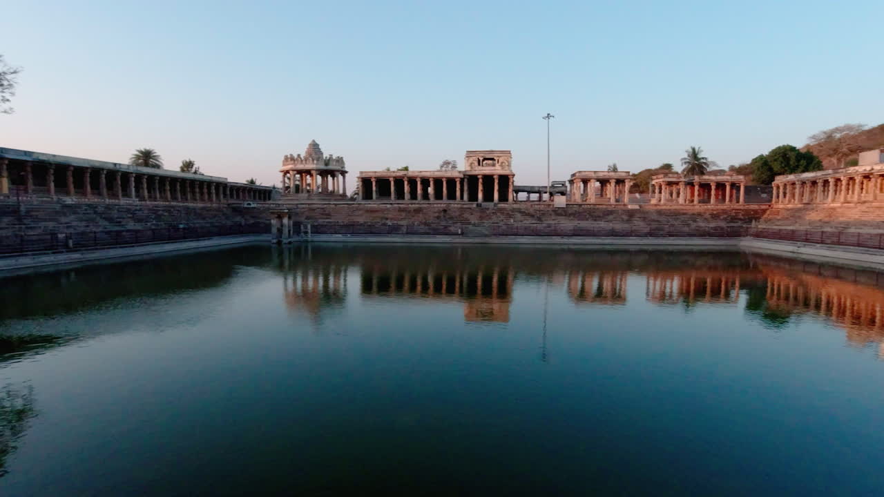 Plan panoramique lent de l'historique bassin à degrés de Kalyani, des couloirs en pierre, du dôme du Mantapa de Bhuvaneshwari et du temple de Yoga Narasimha Swamy au coucher du soleil, à Melukote, Karnataka.