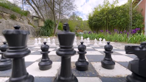 In-the-middle-of-the-courtyard,-a-large-chessboard-is-depicted,-with-chess-pieces-strategically-placed-upon-it