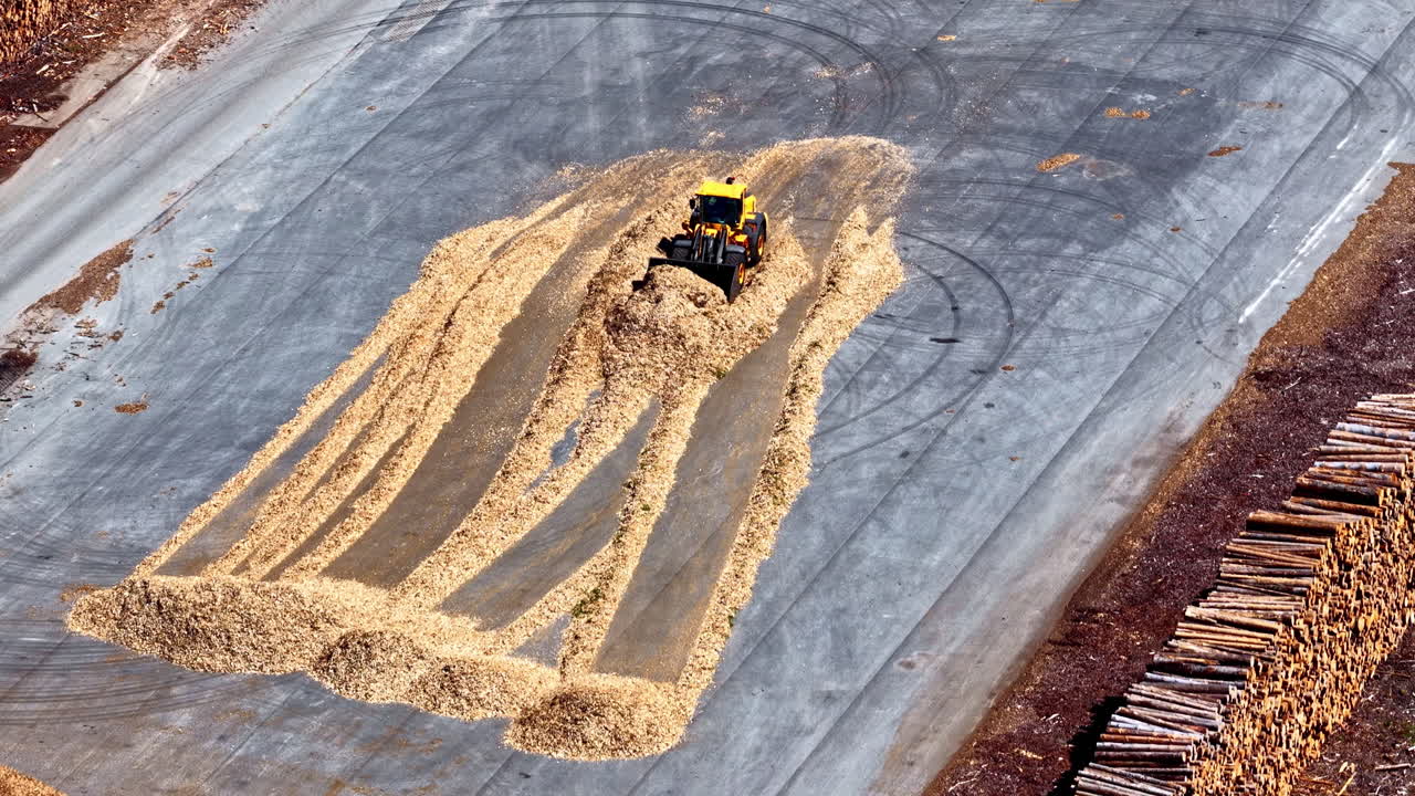 Aerial view of a loader pushing piles of wood chips at Mērsrags Port, Latvia, surrounded by stacks of timber logs