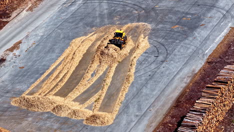 aerial view of a loader pushing piles of wood chips at mērsrags port, latvia, surrounded by stacks of timber logs