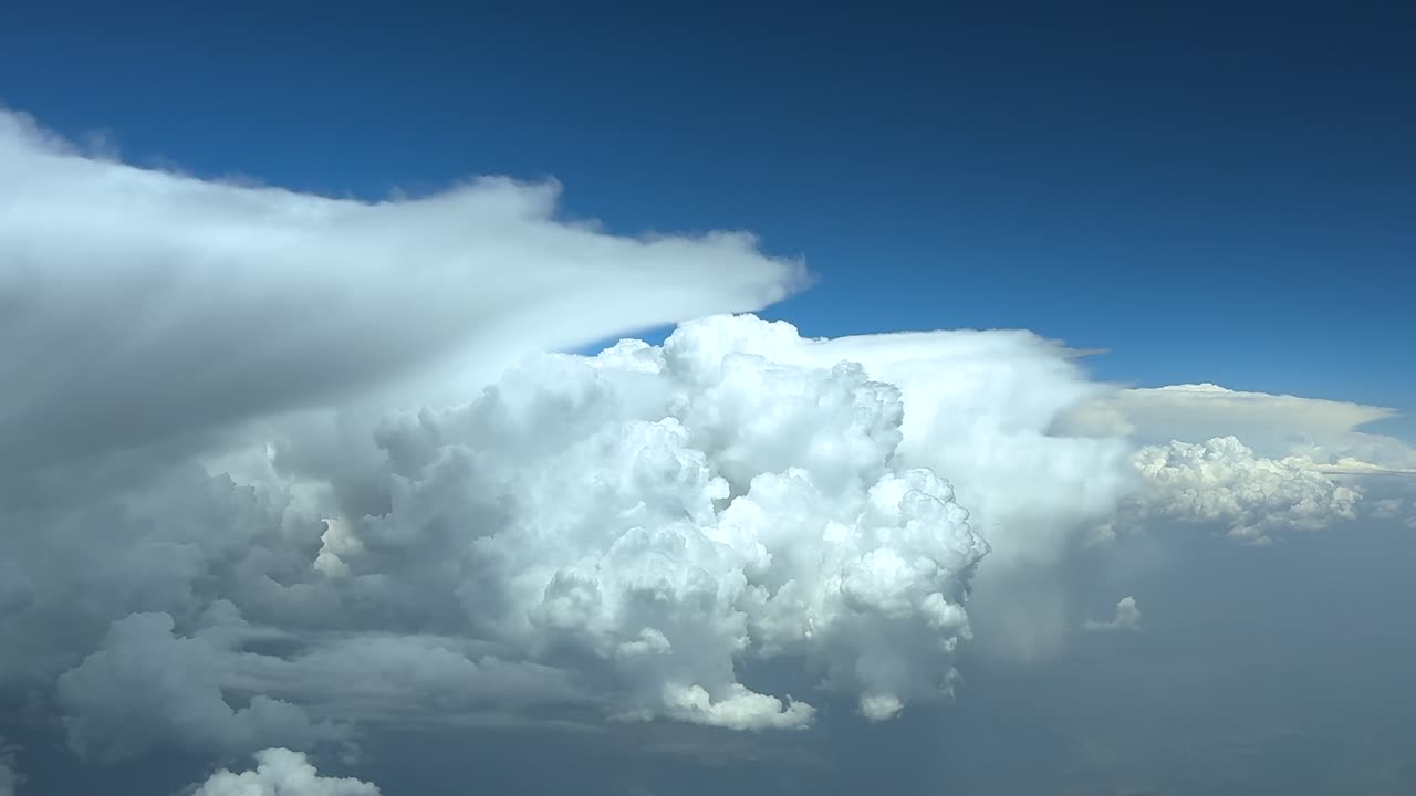 A cloudscape POV take from a jet cockpit, flying peacefully through threatening and dangerous cumulonimbus storm clouds under an intense blue color sky. wide-angle shot, thrUltra-realistic 4K.
