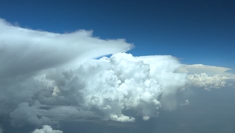 a cloudscape pov take from a jet cockpit, flying peacefully through threatening and dangerous cumulonimbus storm clouds under an intense blue color sky. wide-angle shot, thrultra-realistic 4k.