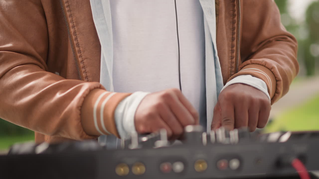 DJ che mixa su controller all'aperto in un parco, artista con giacca casual che regola manopole e fader sotto una calda luce solare, atmosfera estiva rilassata con sfondo di vegetazione, groove ambientale ed energia da evento comunitario.