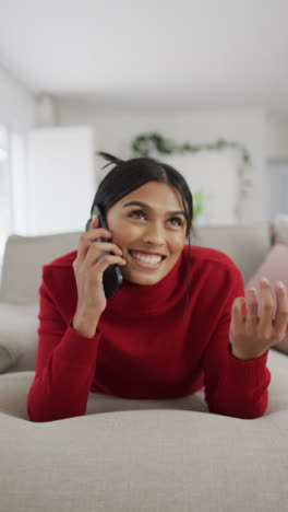 video vertical de una mujer biracial feliz hablando por teléfono en el sofá