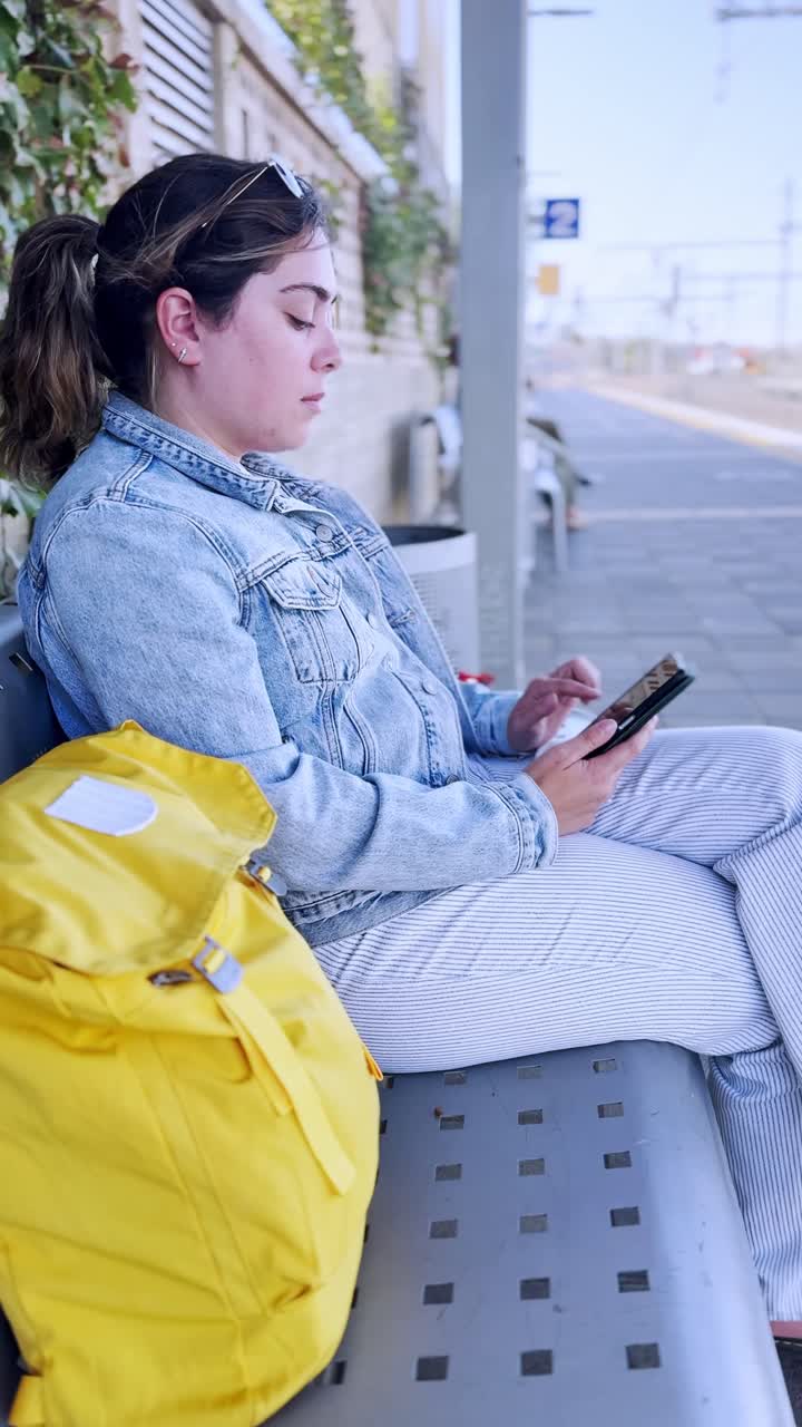 Young Woman Waiting for a Train While Using Her Smartphone at a train station platform