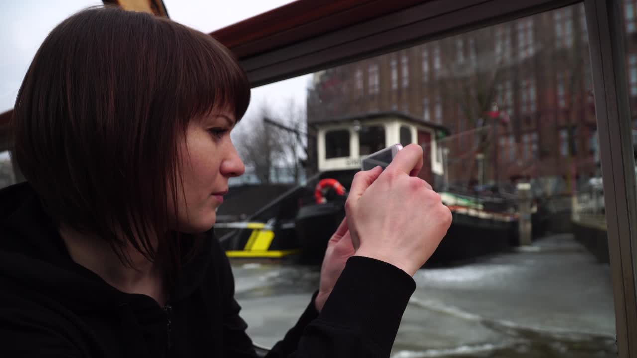 여성은 암스테르담의 운하를 가로질러 배를 타고 전화로 사진을 찍습니다.