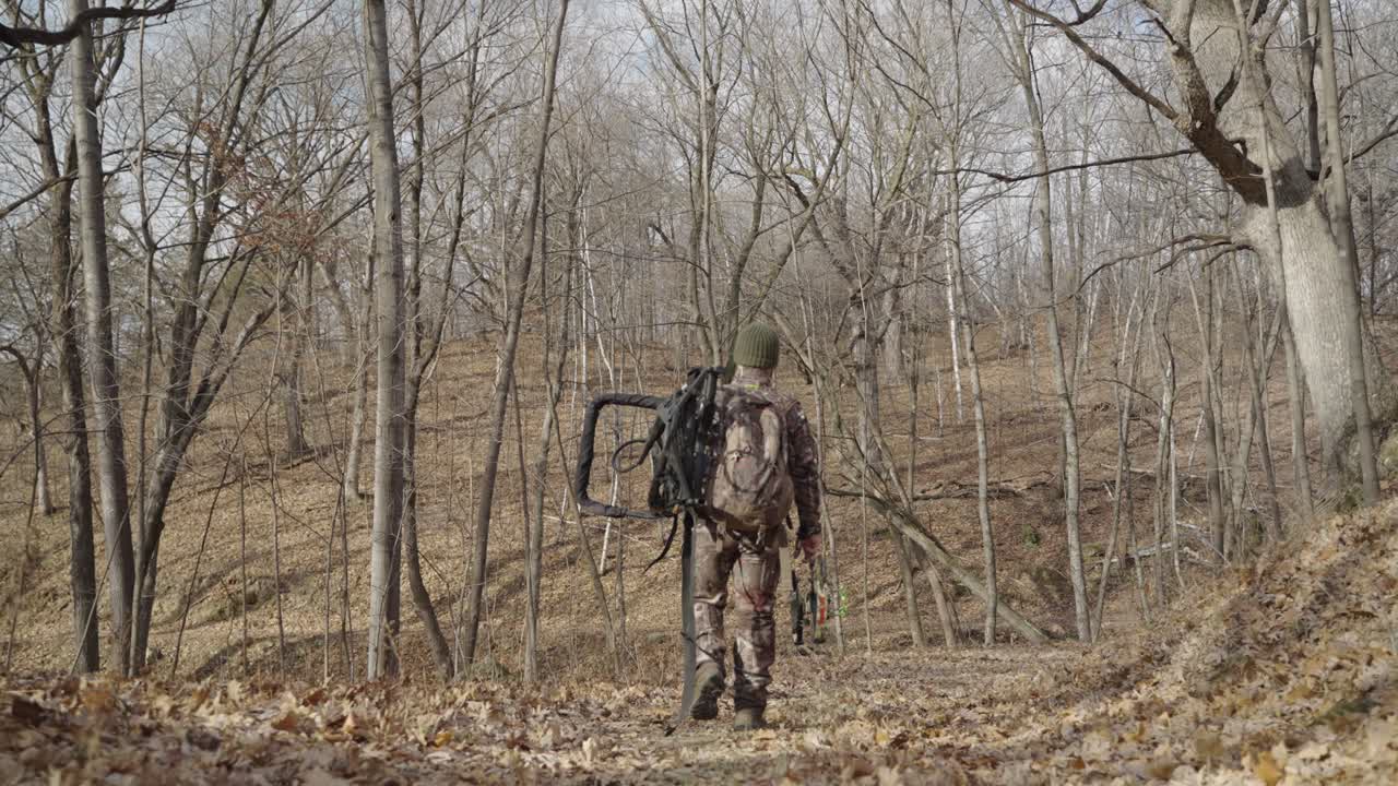 Gimbal following bowhunter holding hunting equipment walking on forest path
