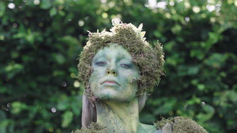 Close-up-of-a-female-model-wearing-green-bodypaint-gesturing-with-her-head-in-a-forest,-in-the-style-of-nature-inspired-forms