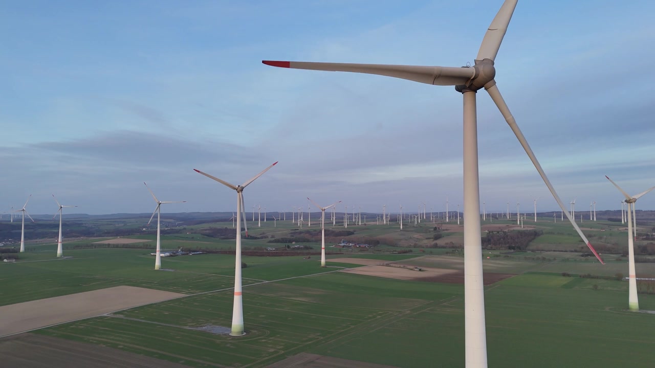 Drone flies very near the blades and arcs around the turbine to reveal the full wind park.