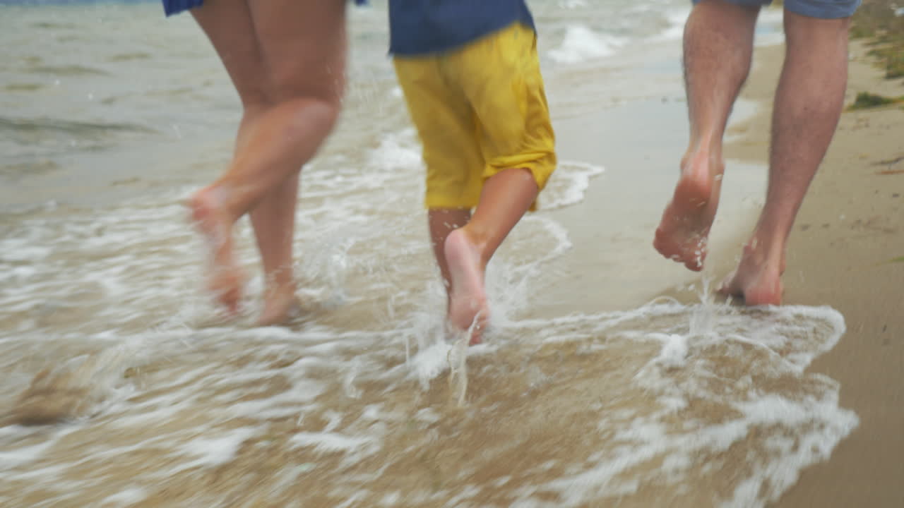 una familia de tres personas divirtiéndose corriendo en la playa.