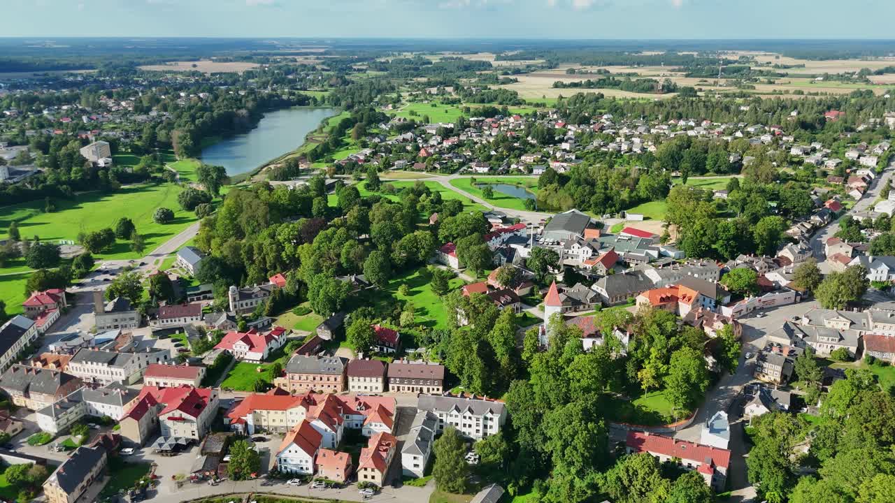 Panoramic view capturing Talsi's historic town center, nestled among verdant landscapes, reflecting traditional Latvian architectural charm beside tranquil lake waters, drone establishing shot