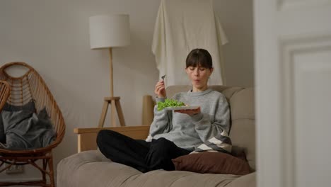 woman eating salad on a sofa at home