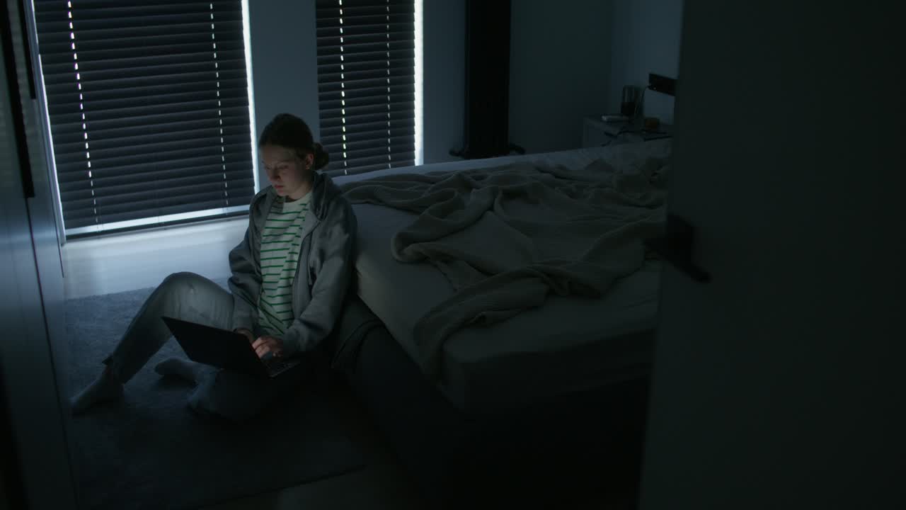 Adolescente che lavora al portatile in una camera da letto buia di notte