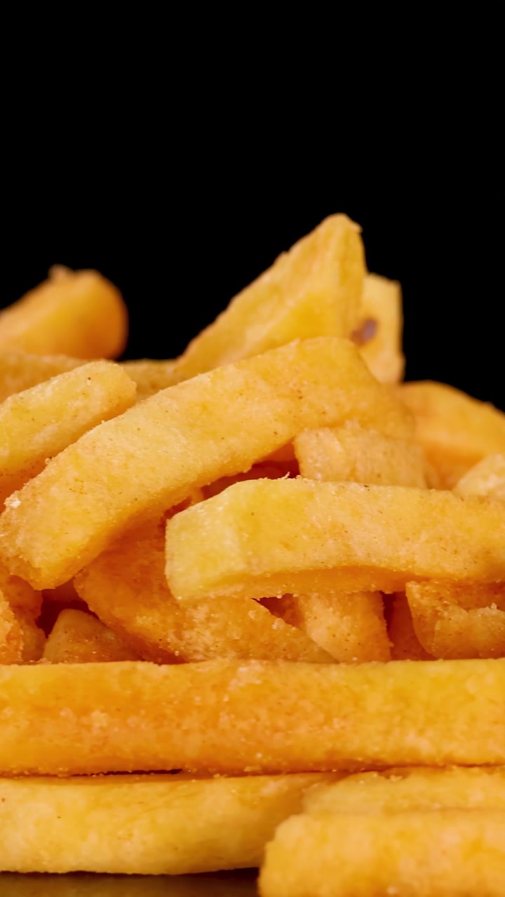 Batatas fritas douradas e crocantes giram em close-up detalhado contra um fundo preto, com iluminação dramática.