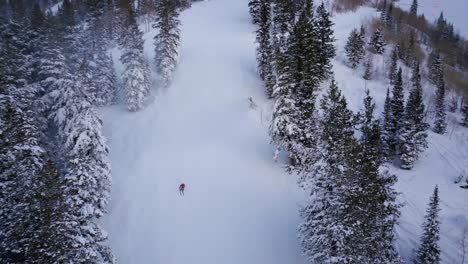 skiers and snowboarders race down the side of a snow packed mountain side in utah