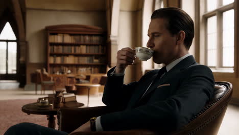 a man in a suit sips tea in a sophisticated study or library