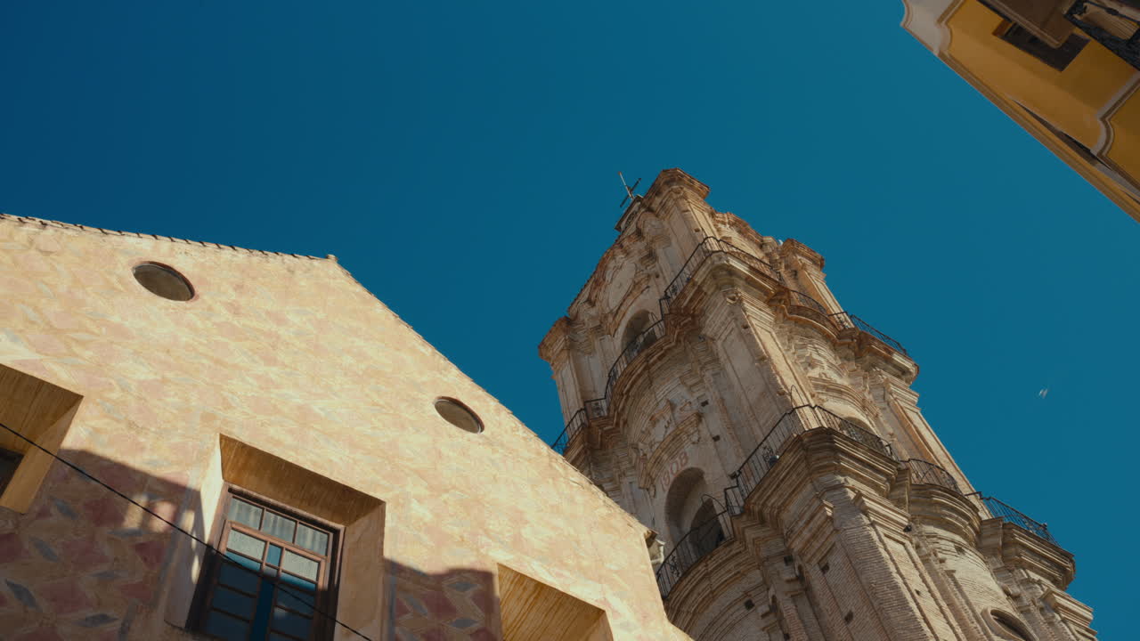 Drammatica inquadratura dal basso della torre della Cattedrale di Malaga che si erge contro un cielo azzurro chiaro in Andalusia, Spagna. Architettura barocca storica catturata sotto la calda luce del sole mediterraneo
