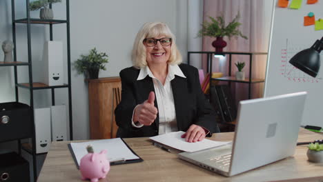 senior business woman raises thumbs up, agrees, approve, likes good news using laptop at home office