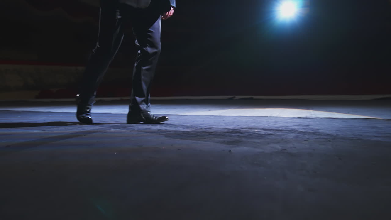 Male's legs on stage. Man actor in trousers and black shoes dancing on stage. Close-up.