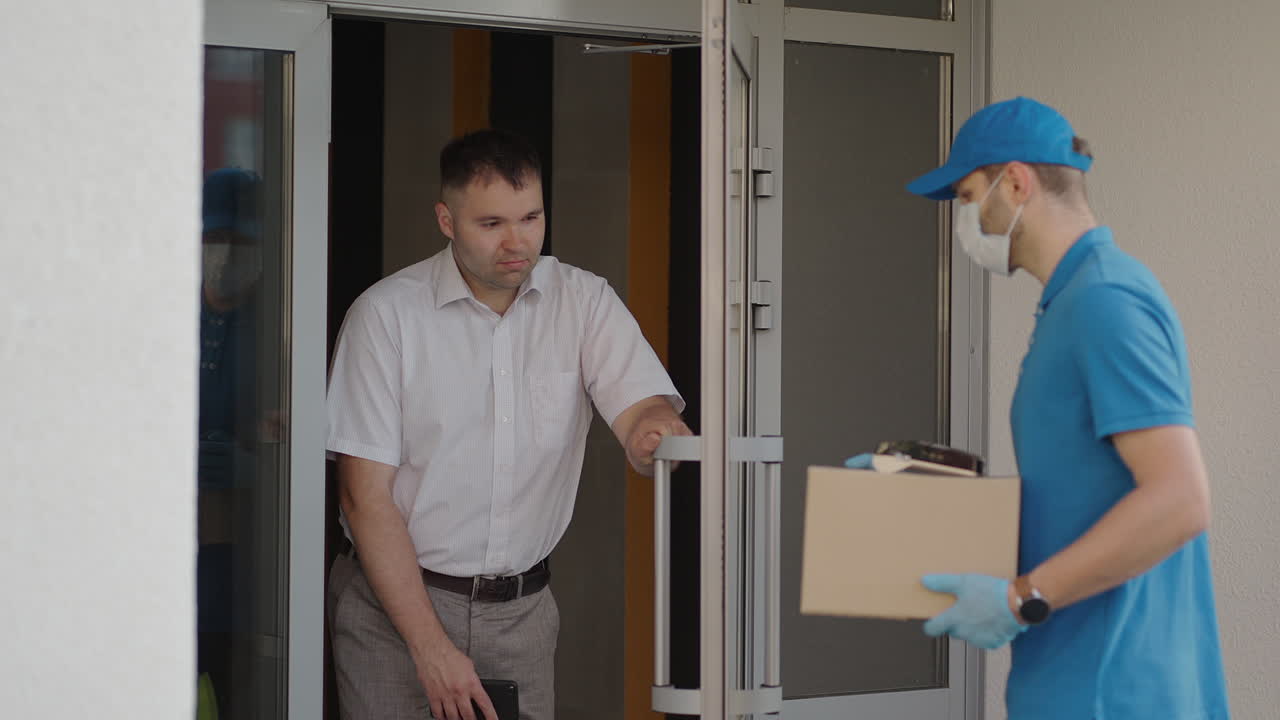 мужчина-доставщик в масках и защитных перчатках доставляет посылку клиенту с терминалом для бесконтактной оплаты по мобильному телефону или карте nfc.