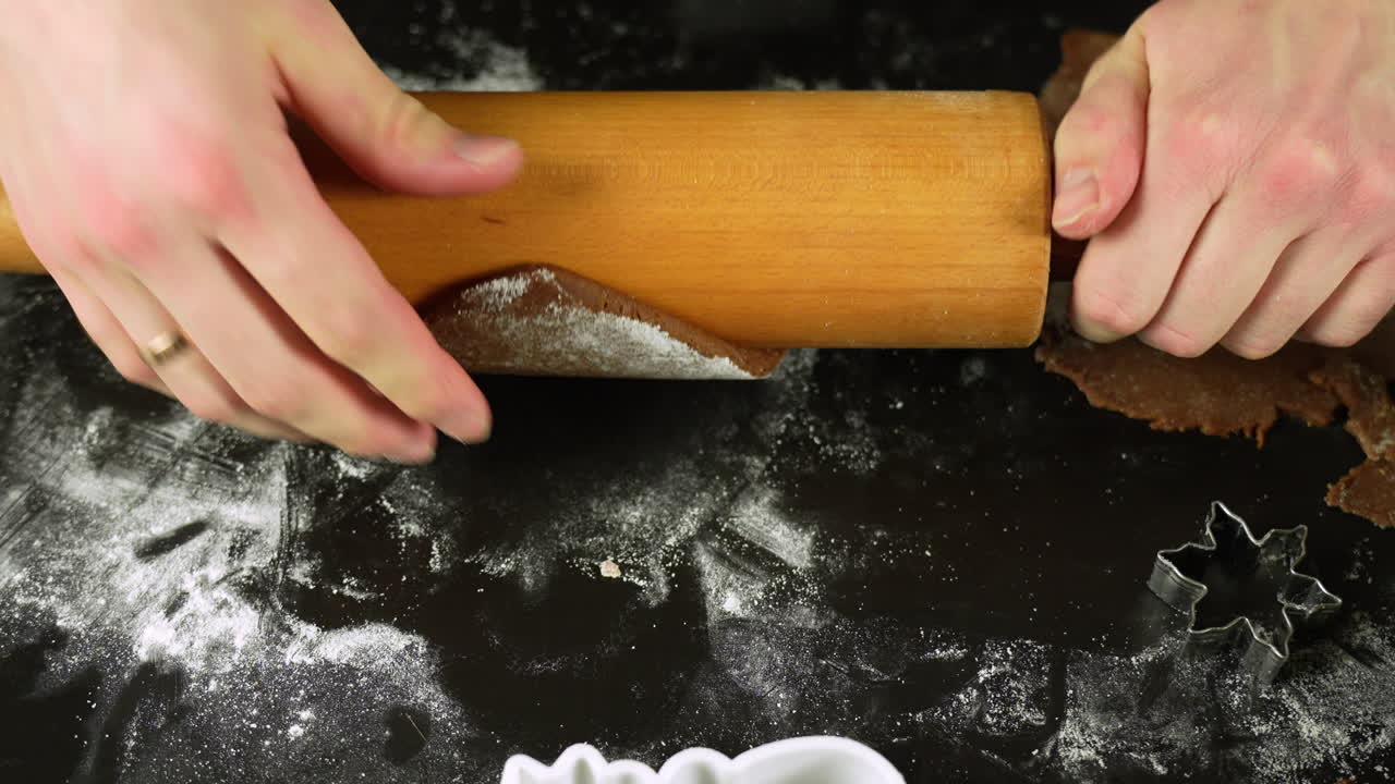 Mom flattening gingerbread dough with hand, next to wooden rolling pin and star shaped cookie cutter, making Christmas cookies with her child